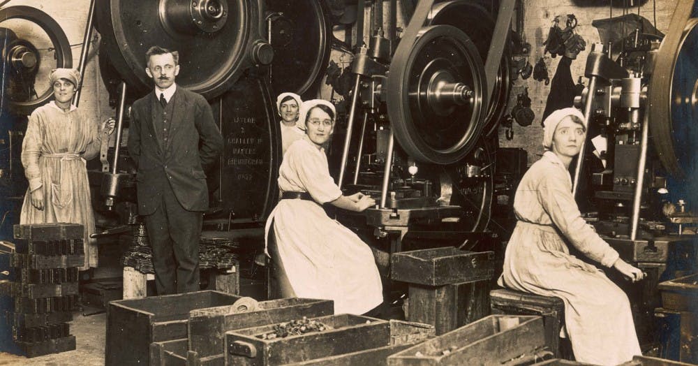 Old black and white photograph of 4 female workers wearing white dresses as uniforms and male supervisor in a suit in a Manchester munitions factory dated 1918